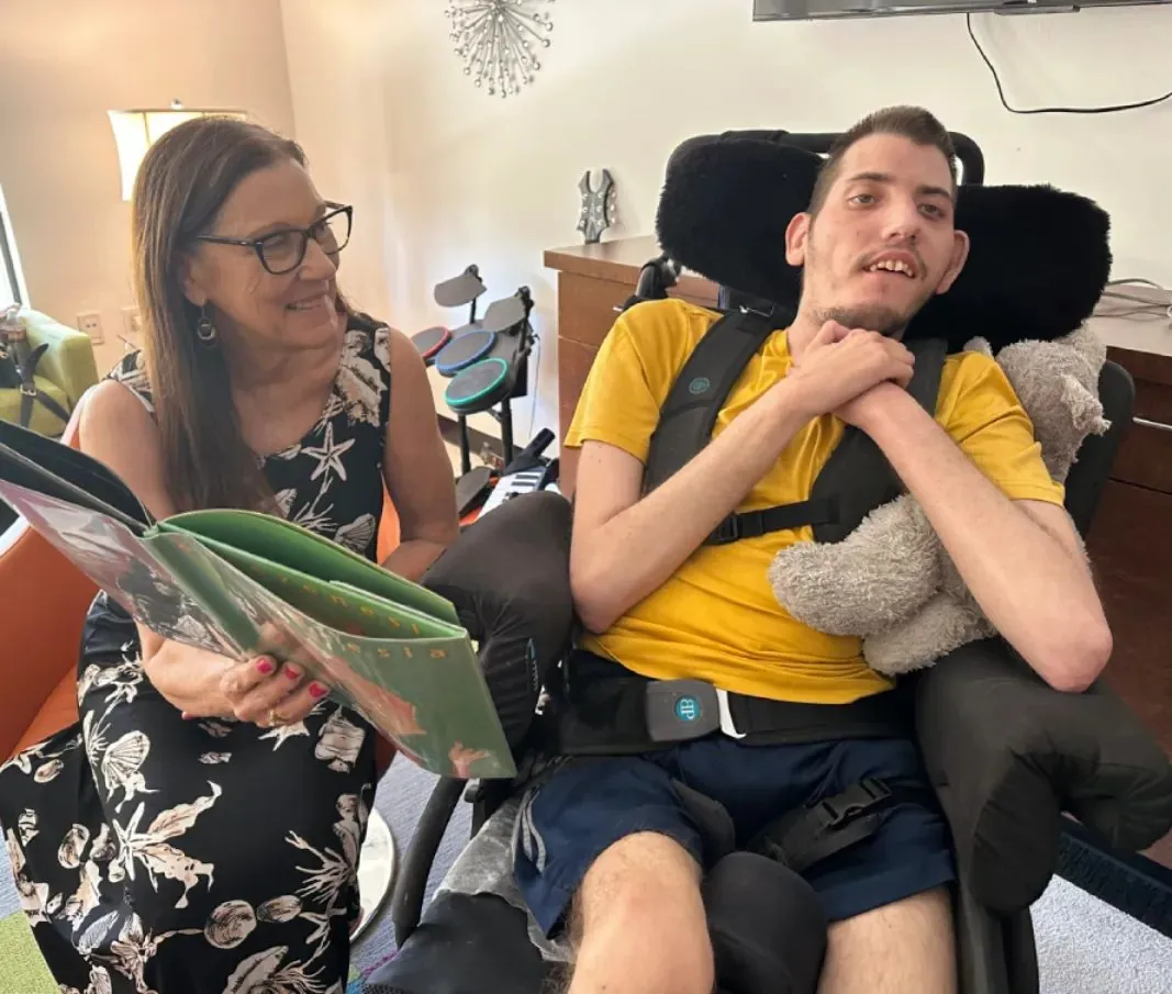 A staff member reading to a participant during a school to adult day programs activity at Cortney's Place