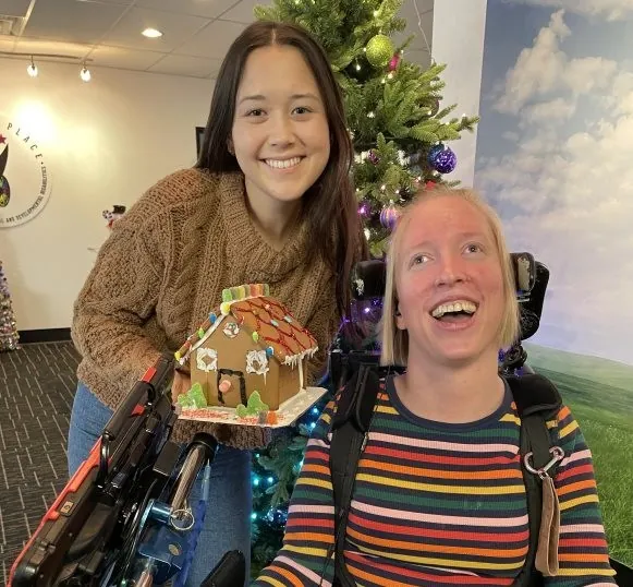 Adult with IDD smiling with a gingerbread house made during a creative program