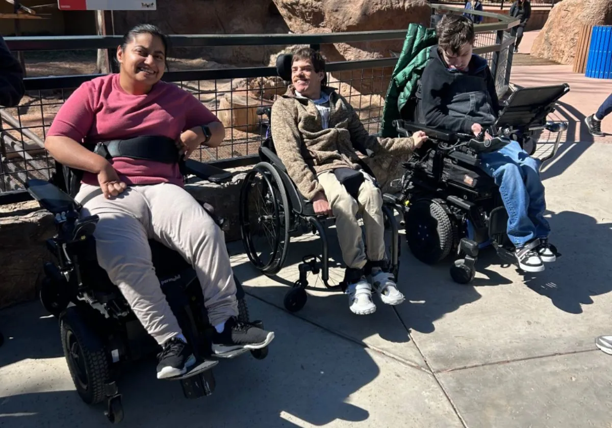 Adults with IDD on a community outing at the zoo, smiling outdoors in wheelchairs