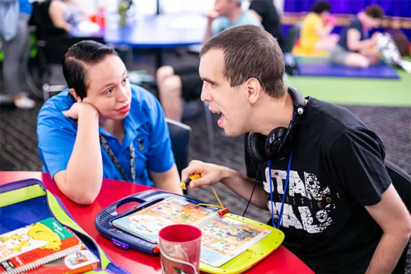 Adult with IDD using a communication device during a community participation activity with a support staff member